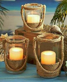 three lit candles sitting on top of a wooden table next to a basket with seashells