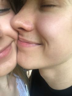 two women who are kissing each other with their noses close to one another and looking at the camera