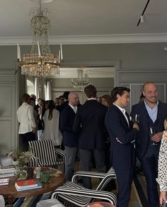 a group of people standing in a living room next to a table with wine glasses on it