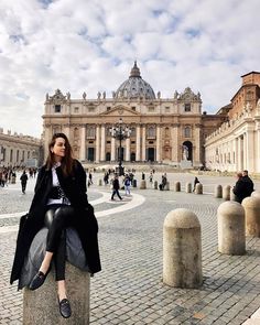 a woman sitting on top of a stone pillar in front of a building with a dome