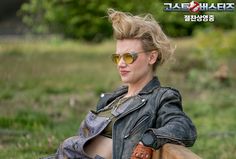 a woman wearing sunglasses sitting on top of a wooden bench next to a field and trees