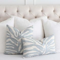 three zebra print pillows sitting on top of a white bed with tufted headboard