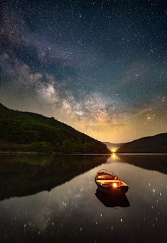 a small boat floating on top of a lake under a night sky filled with stars