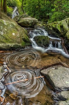 a small waterfall in the middle of a forest filled with rocks and water flowing down it's sides