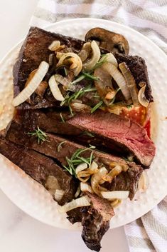 a white plate topped with steak, mushrooms and onions on top of a table cloth