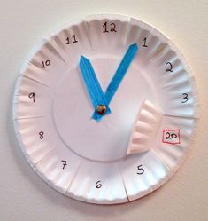 a paper plate clock with blue hands and numbers on the face is mounted to a wall