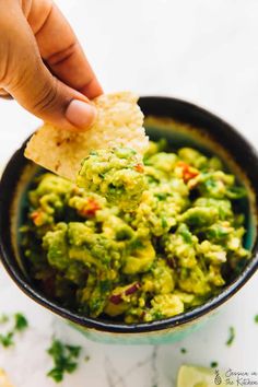 a hand holding a tortilla chip over a bowl of guacamole