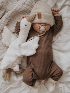 a baby laying on top of a bed next to a white stuffed animal and wearing a hat