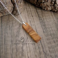 a wooden necklace with a silver chain on a wooden surface next to a tree trunk