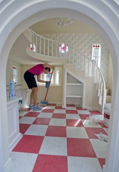 a woman is cleaning the floor with a mop in her hand while standing on a red and white checkered tile floor