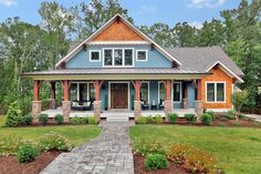 a blue and brown house with lots of trees in the front yard, walkway leading up to it