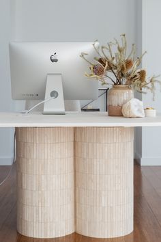 an apple computer sitting on top of a wooden desk next to a vase with flowers