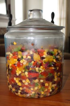 a glass jar filled with lots of different colored veggies on top of a wooden table