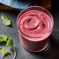 a smoothie is shown in a glass on a table next to some green leaves