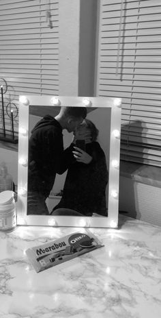 a black and white photo of a couple kissing in front of a mirror with lights