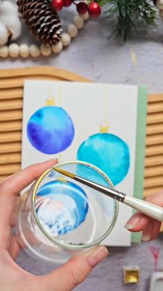 someone is painting christmas ornaments with watercolors on paper and using a paintbrush