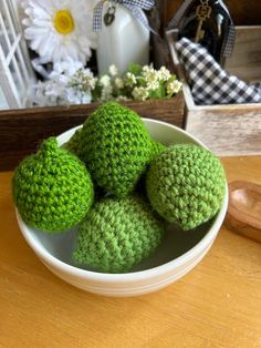 four green crocheted balls sit in a bowl on a table next to flowers