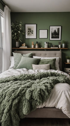 a bed with green blankets and pillows in front of two framed pictures on the wall