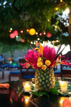 a pineapple centerpiece with flowers and candles on a table in front of lights