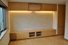 an empty room with wooden flooring and built in storage units next to a window