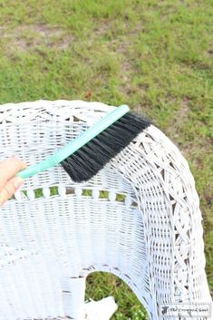 a person holding a brush on top of a wicker chair in the grass,