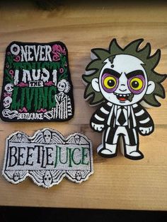 three patches sitting on top of a wooden table next to each other, one with the word beetlejuice