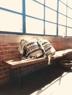 a wooden bench with blankets on it in front of a brick wall and large windows