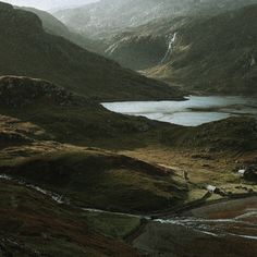 the mountains are covered in green grass and there is a body of water surrounded by hills