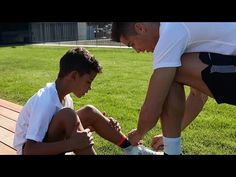 two young men sitting on top of a wooden bench next to each other in the grass