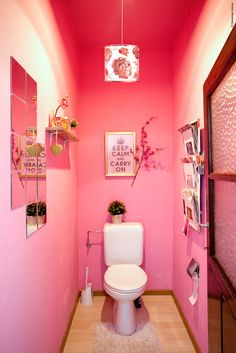 a bathroom with pink walls and white toilet in the center, decorated with pictures on the wall