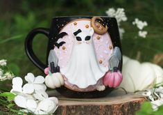 a black coffee mug with a white ghost and two birds on it, surrounded by flowers