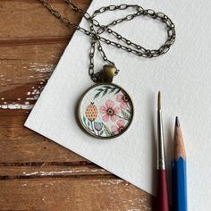 a necklace with flowers and pineapples on it next to a pair of pencils