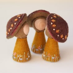 two small mushrooms made out of felt on a white surface with tiny flowers and leaves