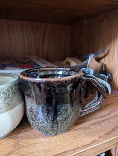 two mugs sitting on top of a wooden shelf