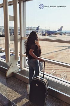 a woman standing next to an airport window with her luggage