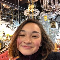 a woman is smiling in front of chandeliers and other items hanging from the ceiling