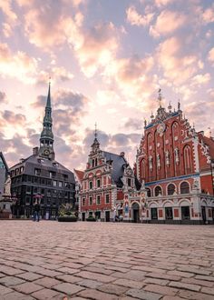 an old town square with many buildings and a clock tower in the background at sunset