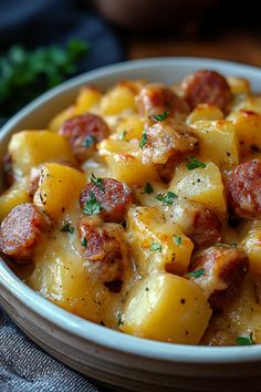 a white bowl filled with potatoes and sausage on top of a blue table cloth next to some parsley