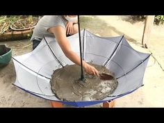 a woman in grey shirt holding an umbrella over a metal pan with dirt on it