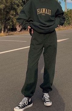 a woman standing in the middle of a street wearing a green sweatshirt and sweatpants