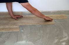 a person laying wood on the floor with their feet in the air and one hand reaching for it