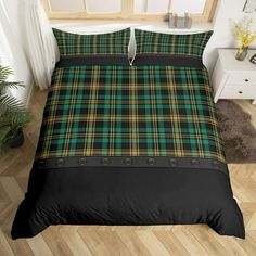 a green and black plaid bed set on a wooden floor next to a potted plant