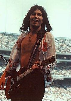 a man with long hair playing an electric guitar in front of a large stadium full of people