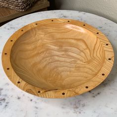 a wooden bowl sitting on top of a white marble table next to a brown basket