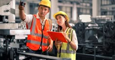 two people in safety vests and hard hats are looking at something on a clipboard