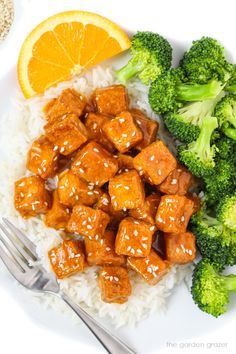 a plate with rice, broccoli and tofu next to an orange slice