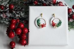 a pair of earrings sitting on top of a white box next to some red berries