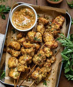 chicken skewers on a tray with dipping sauce and parsley sprigs