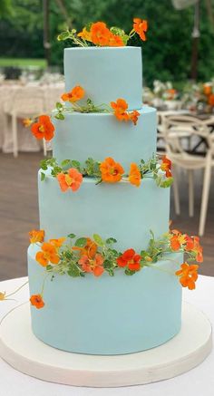 a three tiered blue cake with orange flowers on it