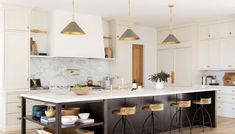 a kitchen with marble counter tops and gold pendant lights hanging from the ceiling over the island